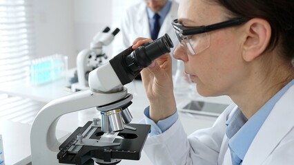 Female scientist examining sample under microscope, conducting research in laboratory with...