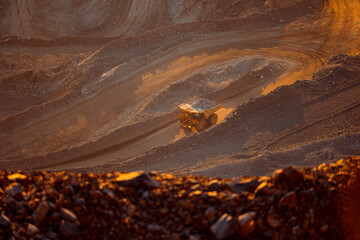 Mining big yellow Dump Truck Navigating Dusty Terrain in sunset light.