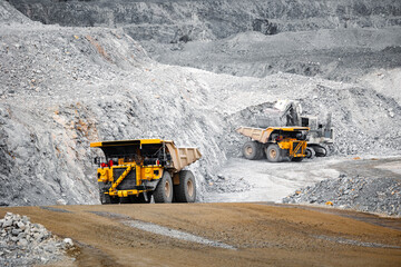 Large Dump Trucks with ore Navigating Wide Roads in Massive Open-Pit Mine of gold.