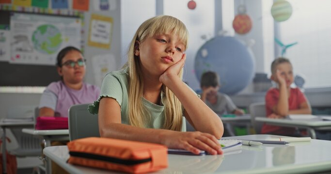 Sad Primary School Girl Sitting at Desk, Getting Tired During Lesson or Upset Because of Bad Grade on Homework. Group of Young Children Learning Science or Geography in Modern Classroom. Dolly Shot. - Powered by Adobe