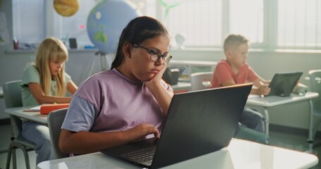 Computer Science Lesson: Primary School Girl Sitting at Desk, Using Laptop in Classroom. Group of...