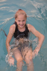 Joyful girl in a black swimsuit smiles in a swimming pool