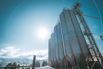 Large industrial grain silos of a feed mill facility stand against a clear blue sky in rural Spain,...
