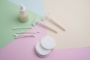 White razor with cotton pads and sticks, face cream or serum on pastel background. Self-hygiene,...