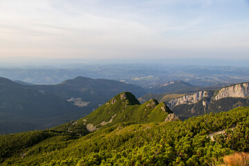 Green mountain ridge with distant cliffs and panoramic valley view under warm sunset light.