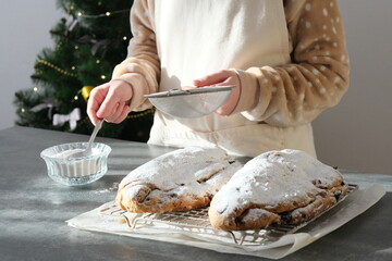 A person in a cozy kitchen prepares freshly baked pastries, dusting them with powdered sugar while...