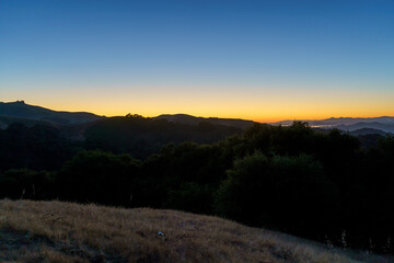 Layers of hills are silhouetted against a serene sky transitioning from deep blue to a warm, golden glow at dusk.
