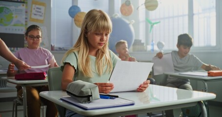 Teacher Giving Papers with School Test Results to Primary School Children Sitting at Desks in...