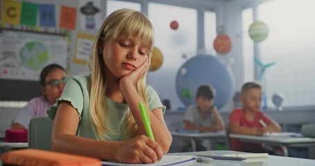 Primary School Girl Sitting at Desk, Raising Hand and Reading Correct Answer from Notebook During...