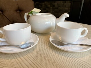 a white teapot with tea and two mugs are on the table
