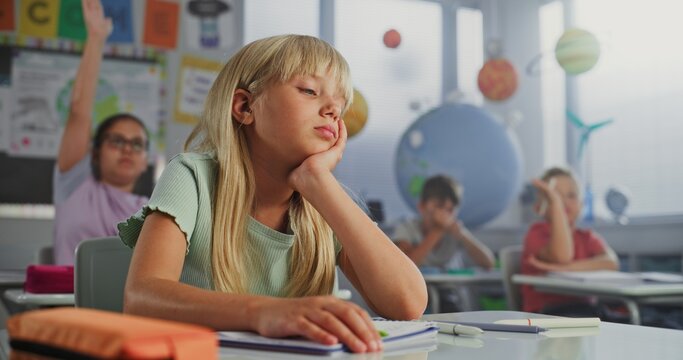 Depressed Elementary School Girl Sitting at Desk, Getting Upset About Bad Grade on School Test or Bored During Lesson. Team of Smart Diverse Kids Studying Environmental Science in Modern Classroom.