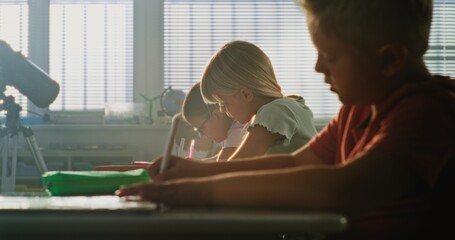 Primary School Children Sitting at Desks, Writing School Exam or Doing Tasks in Notebooks. Group of...