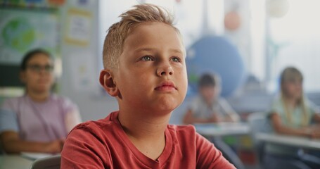 Close Up of Elementary School Boy Sitting at the Desk, Listening to Lecture from Teacher During Geography Lesson. Team of Smart Diverse Kids Studying Environmental Science in Modern Colorful Classroom
