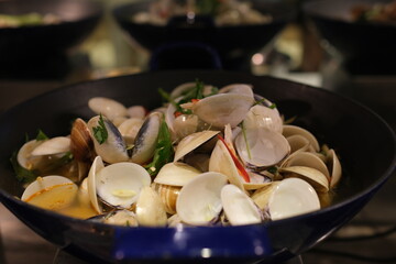 Fresh clams being steamed in a pan on a stovetop, preparing spaghetti or linguine. The clams are...