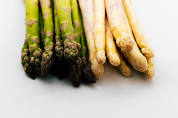Fresh green and white asparagus arranged side by side on a clean surface during bright lighting