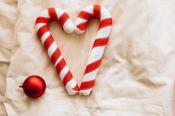Candy canes shaped like a heart with a red ornament on a soft textile background