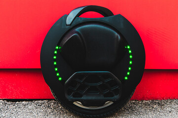 Electric unicycle parked near a red wall on a bright day with green lights illuminated