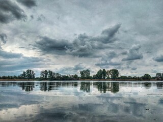 Dramatic cloudy sky reflected in a calm lake with a tree line on the horizon. Peaceful nature...