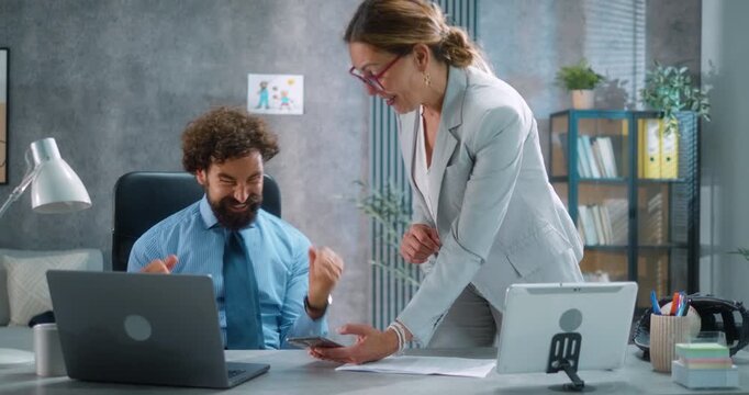 Excited female assistant brings good news to the business manager, showing phone with successful financial results. Office celebration, achievement, and good business news. Part 34 of the “Dad’s Day” 