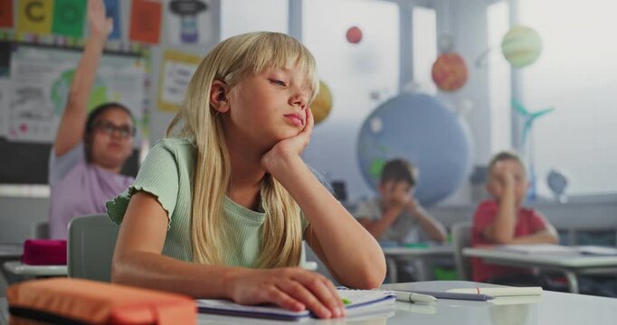 Depressed Elementary School Girl Sitting at Desk, Getting Upset About Bad Grade on School Test or Bored During Lesson. Team of Smart Diverse Kids Studying Environmental Science in Modern Classroom.