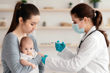 Obraz premium Children Vaccination Concept. Doctor In Medical Mask Doing Immunity Strengthening Injection For Newborn Baby At Home, Holding Syringe, Vaccinating Infant Child While Mother Keeping Him