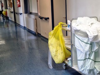 Hospital hallway with laundry cart carrying linens and yellow medical waste bag