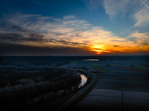 Aerial view of a river snaking through a landscape, where the setting sun paints the sky with fiery hues, National Park Lobau, Witzelsdorf, Lower Austria, Austria.
