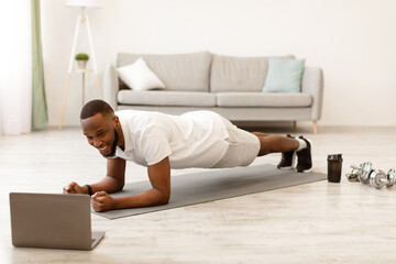 Online Workout. African Guy Exercising At Laptop Standing In Plank Position Training At Home....