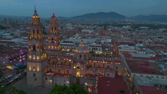 Morelia, Mexico: Beautiful aerial shots around Morelia Cathedral at nightfall. The exterior lights of its bell towers come on, illuminating it aesthetically.