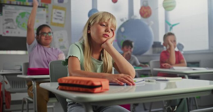 Sad Primary School Girl Sitting at Desk, Getting Tired During Lesson or Upset Because of Bad Grade on Homework. Group of Young Children Learning Science or Geography in Modern Classroom. Dolly Shot.