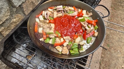 Authentic spanish paella cooking outdoors with fresh ingredients. Typical cuisine of Spain. Valencian cuisine. Stage of cooking paella. Ingredients for paella