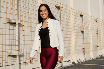 Happy businesswoman walking near a wire mesh fence in the city
