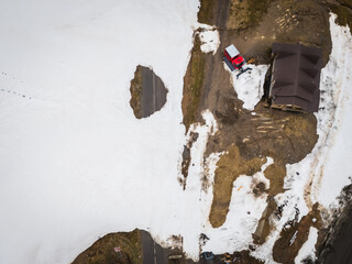 Aerial view of a solitary red snowcat parked near a building amidst melting snow, marking the transition from winter to spring, Goderdzi, Adjara, Georgia.
