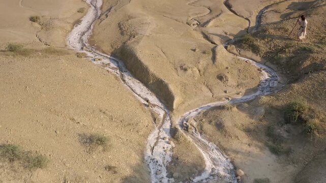 Mysterious man in white robe following dry stream through arid hills in Holy Land. Revealing shot