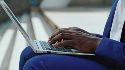 Closeup view of African American man hands write report on laptop in urban area. Entrepreneur prepares digital document for deal agreement sitting on steps during break closeup - Powered by Adobe