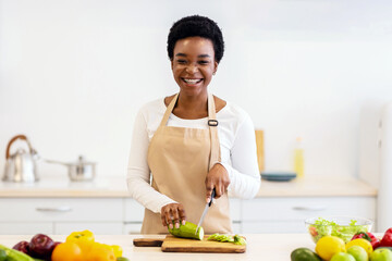 Happy African American Housewife Cooking Cutting Zucchini Vegetable Standing In Kitchen At Home, Wearing Apron. Healthy Eating And Nutrition, Household And Dinner Preparation Concept