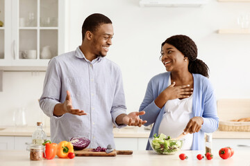 Happy young pregnant black family husband and wife having fun while cooking vegetable salad...