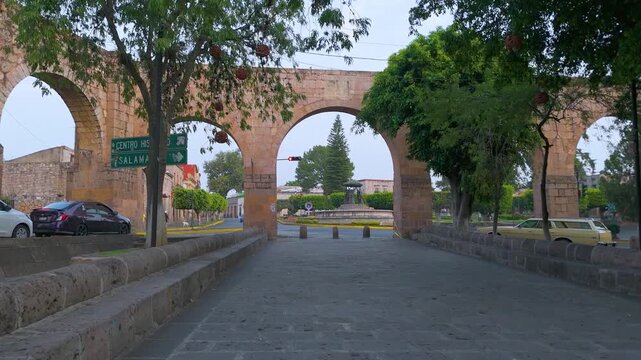 Morelia, Mexico: a calm morning in the capital at the Las Tarascas fountain. The old aqueduct frames the city scene where pedestrians and vehicles begin to bring life to the city.