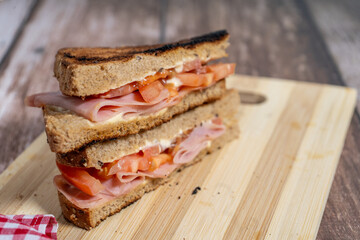 Toasted ham and tomato sandwich resting on cutting board