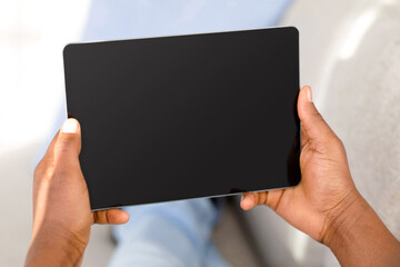 Unrecognizable black man using digital tablet with black blank screen, mockup for application or website advertisement, closeup, crop. Hands holding device with empty space