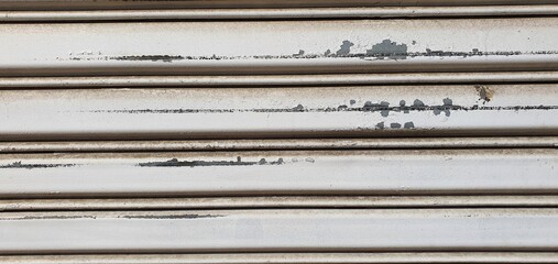Close-up of an old metal rolling shutter with peeling white paint, scratches, rust stains, and weathered texture, showing urban decay and industrial wear
