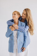 Smiling daughter hugging her beloved mother from behind, wearing matching blue suits