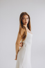 Young woman posing in white dress with long hair looking over shoulder