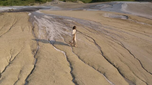 A mysterious man traveling through the dry, sandy mountain hills at sunset holding a wooden staff. Aerial tracking shot