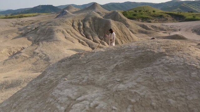 A lone man travelling through the wilderness wearing a white robe. Dolly in revealing shot