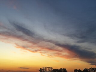 Vibrant evening sky with small clouds shimmering in shades of orange to purple, creating a magical...