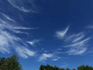 Clear blue sky with delicate, wave-shaped white clouds creating a serene and peaceful atmosphere....