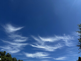 Vibrant blue sky featuring soft, wave-like white clouds gently scattered, offering a dreamy and...