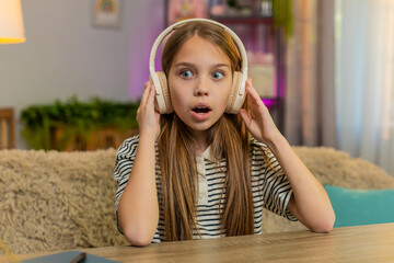 Young child girl sitting at table on home sofa listens to an audio fairy tale in wireless...