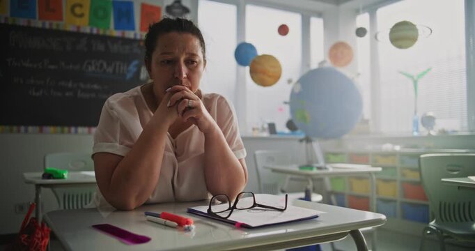 Tired Female Teacher Sitting Alone at the Desk in Empty Classroom, Relaxing After Class. Woman Feeling Stress, Burnout and Mental Exhaustion in Educational Environment, Working in Elementary School.